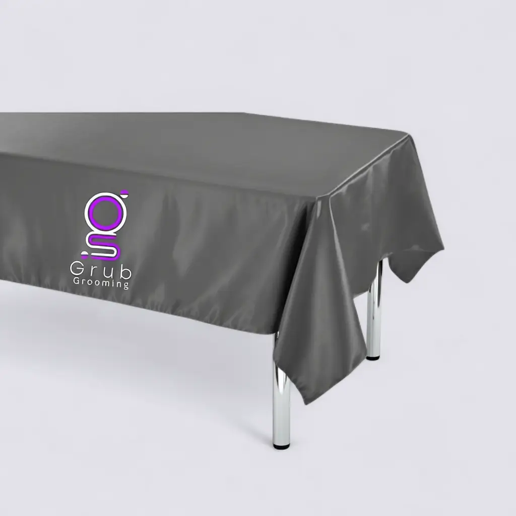 Mantel de presentación gris de GRUB Grooming. Accesorio de presentación con bordado central del logo, diseñado para elevar la percepción profesional del espacio de trabajo. Material satín brillante, bordes doble reforzado y medidas 1.40 m x 0.70 m.