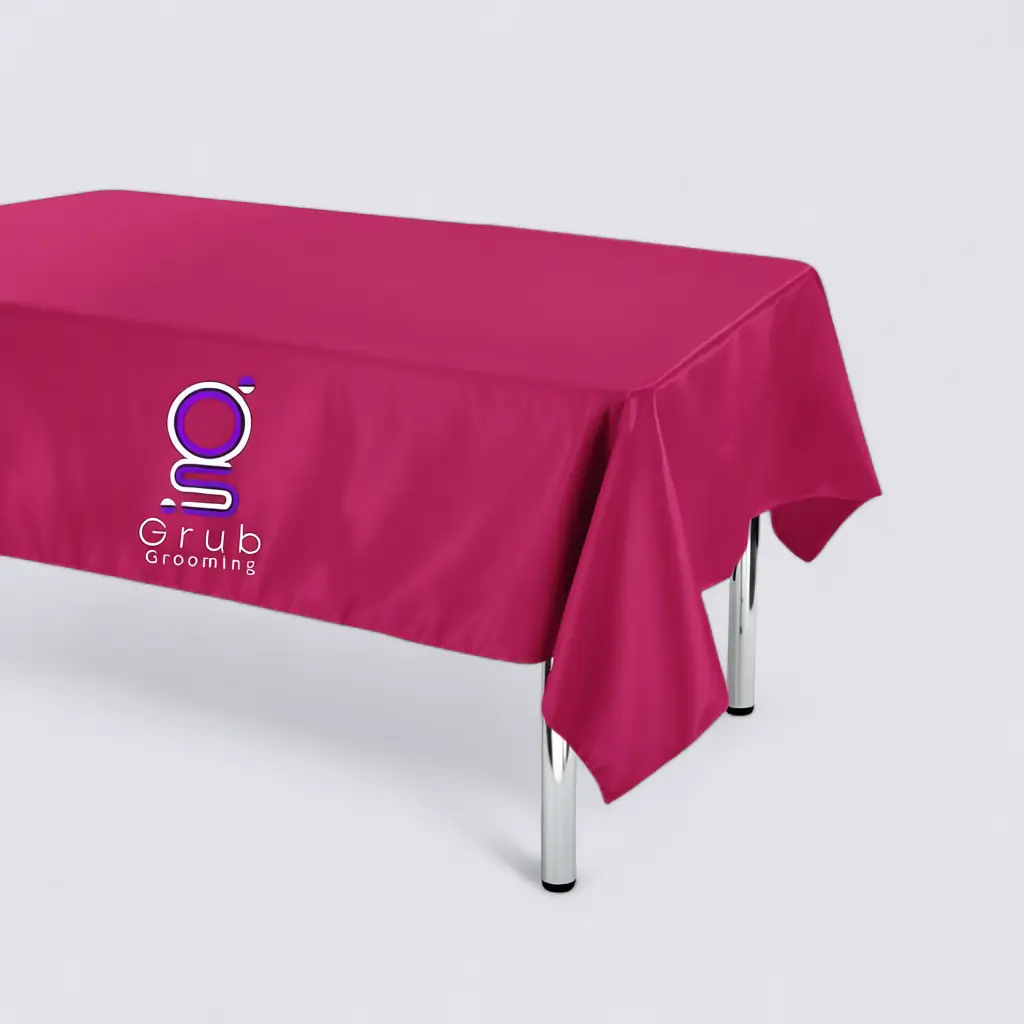 Mantel de presentación rosado de GRUB Grooming. Accesorio sofisticado con bordado central del logo, ideal para ferias o eventos de grooming. Material satín brillante de alta calidad, resistente y fácil de limpiar. Medidas: 1.40 m x 0.70 m.