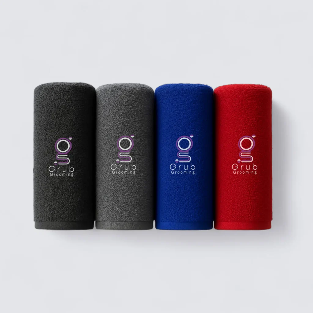 Colección de toallas brandeadas de GRUB Grooming en colores negro, gris, azul y rojo. Toallas de alta absorción diseñadas para el secado profesional de mascotas, con logo bordado en la esquina.